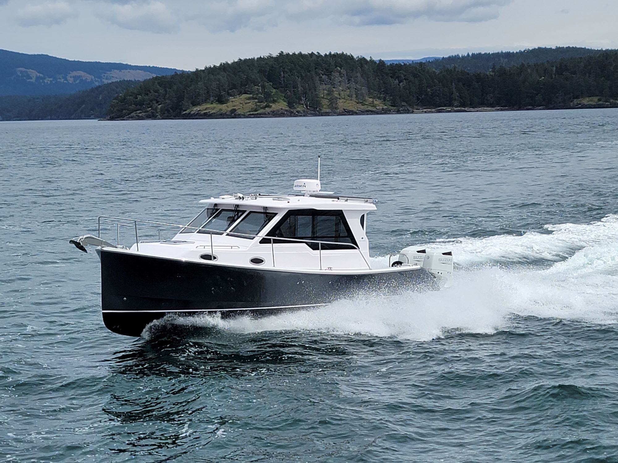 true north 34 outboard express boating on the water in the pacific northwest. trees and land in the background. 